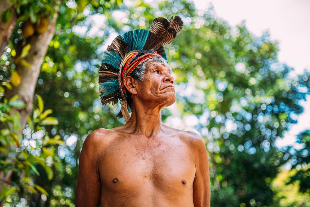 Homem de uma tribo indígena com cocar olhando para o lado